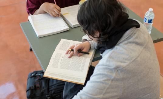 Two students reading books at a square table. 