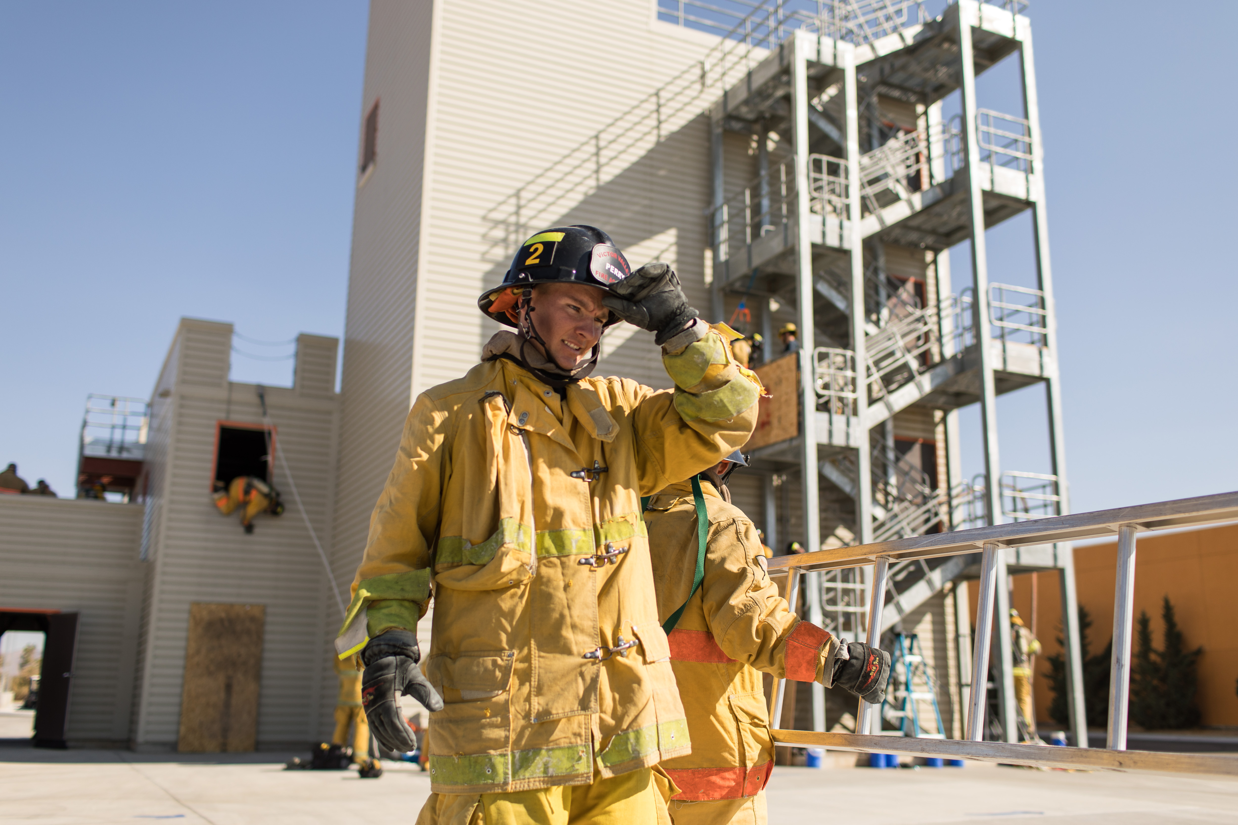 Fire student adjusting his hat while other fire students run drills in the background.