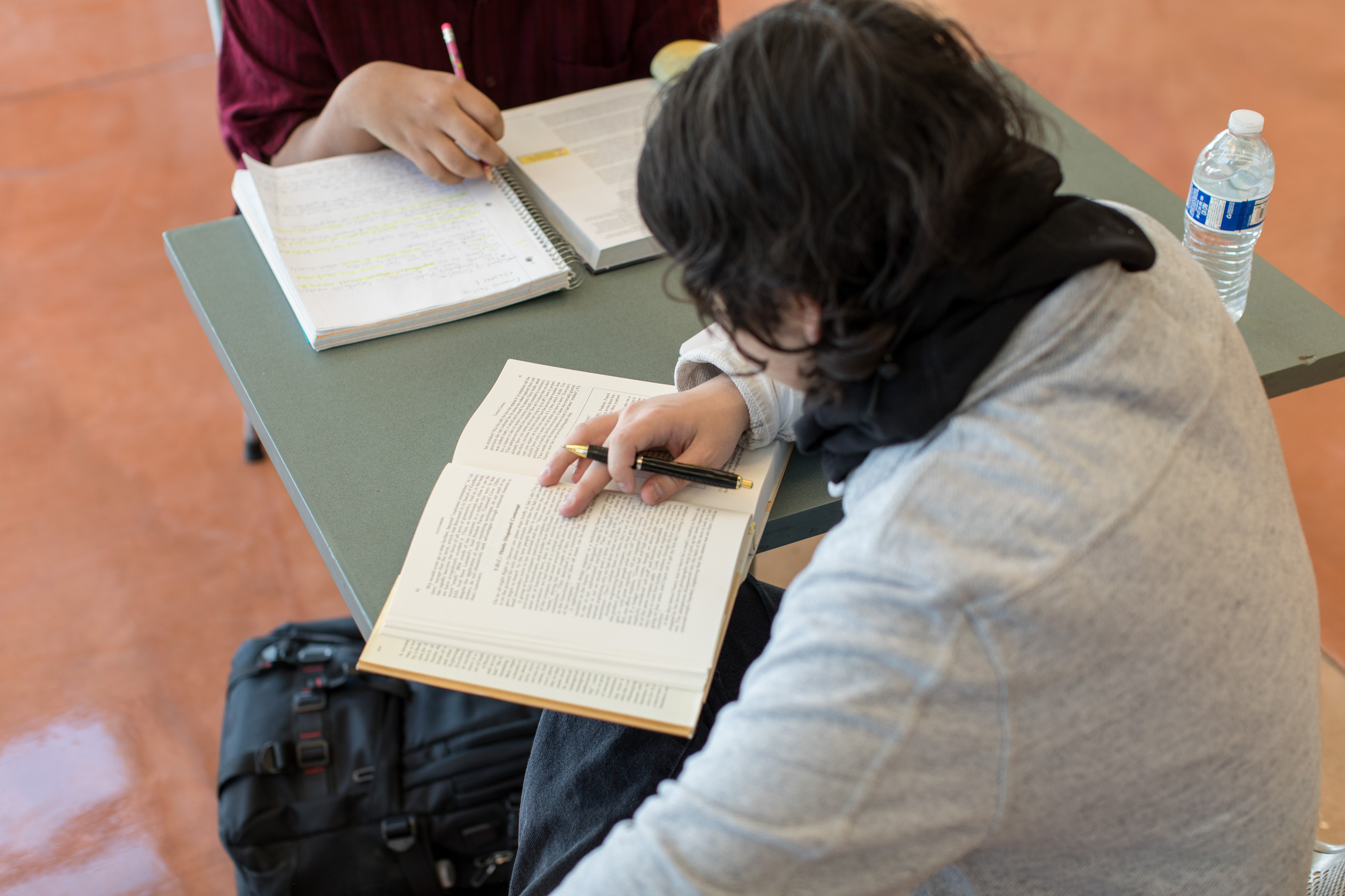 Two students reading books at a square table. 